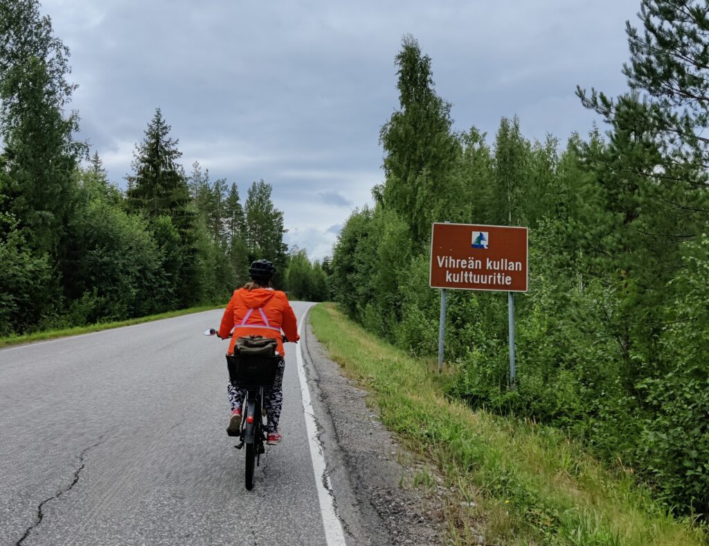Punatakkinen pyöräilijä pyöräilee maantien reunaa pitkin Vihreän kullan kulttuuritiellä. 