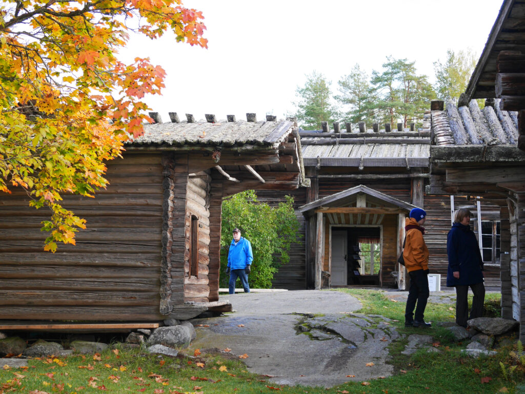 Kuvassa on kolme Pien-Toijolan talonpoikaismuseon museo-aittoaa sekä ihmisiä, jotka tutustuvat aittoihin. Vasemmassa reunassa nahka-aitta oranssinkeltainen vaahtera. Taustalla näkyy päärakennuksen sisäänkäynti.